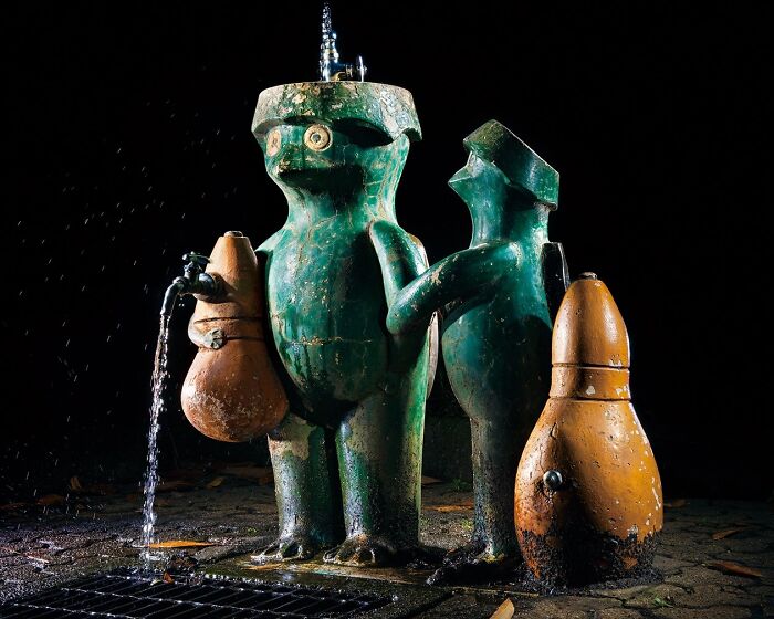 Surreal green frog-like Japanese playground fountain sculptures at night, captured by Fujio Kito, looking like another world scene.