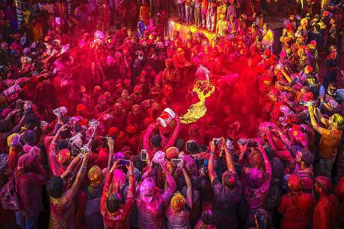 A vibrant crowd celebrates a festival with red powder, highlighting remarkable places and people.