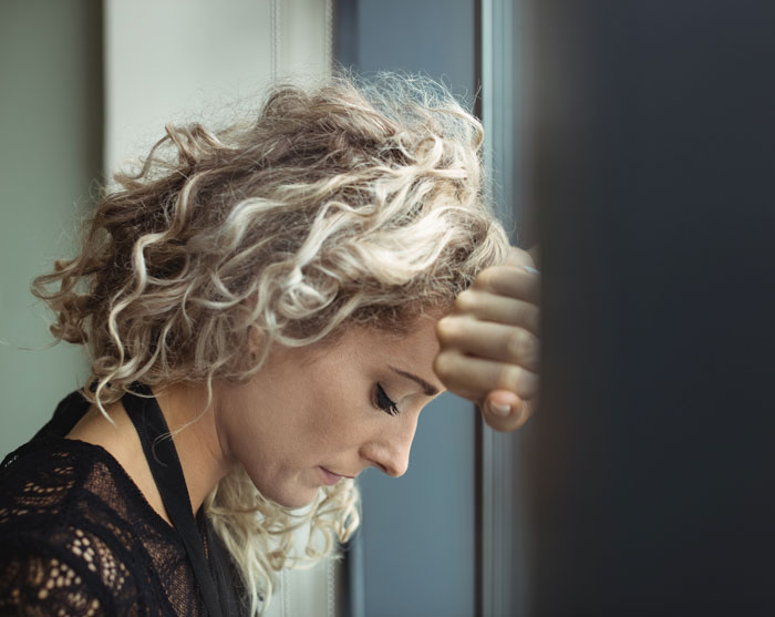 A woman with curly hair, leaning her head against a dark surface, depicting relationship headaches.