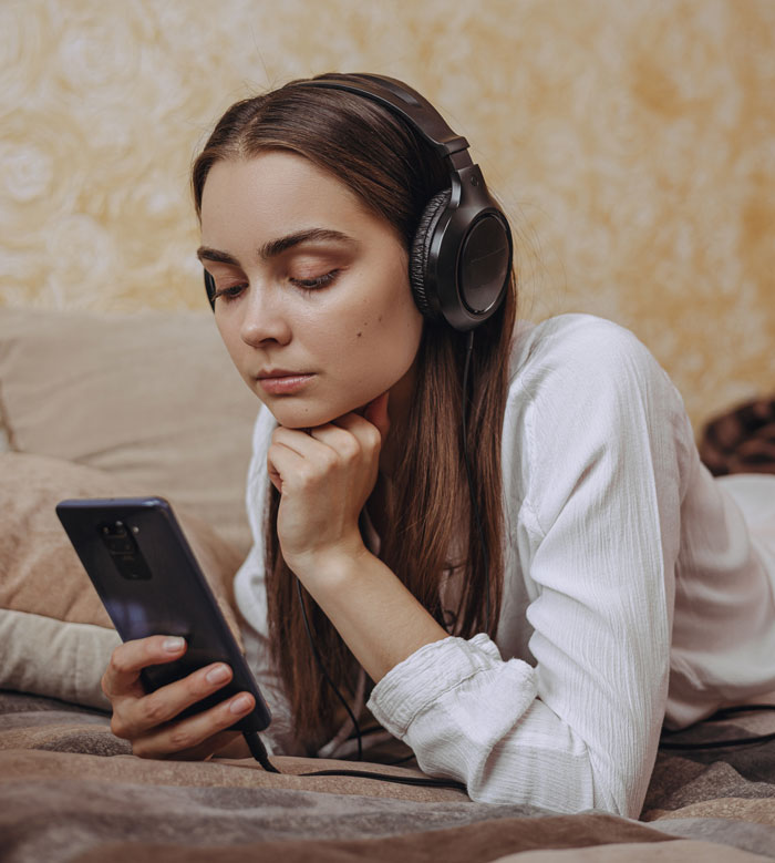 Woman with headphones watching her phone, enjoying stories about women doing crazy things to get a crush to like them.