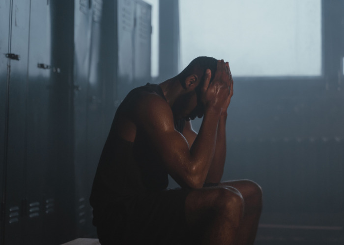 Tired athlete sitting in dark locker room, reflecting on gym phenomenon and physical strain