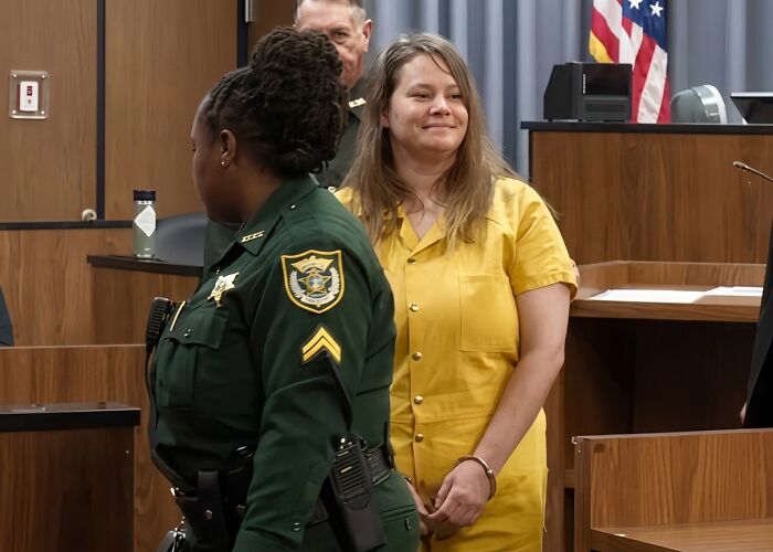 Woman in yellow jumpsuit, handcuffed, smiling in court, identified by her children's father as his attacker in his last words. Woman in yellow jumpsuit, handcuffed, smiling in court, identified by her children's father as his attacker in his last words.