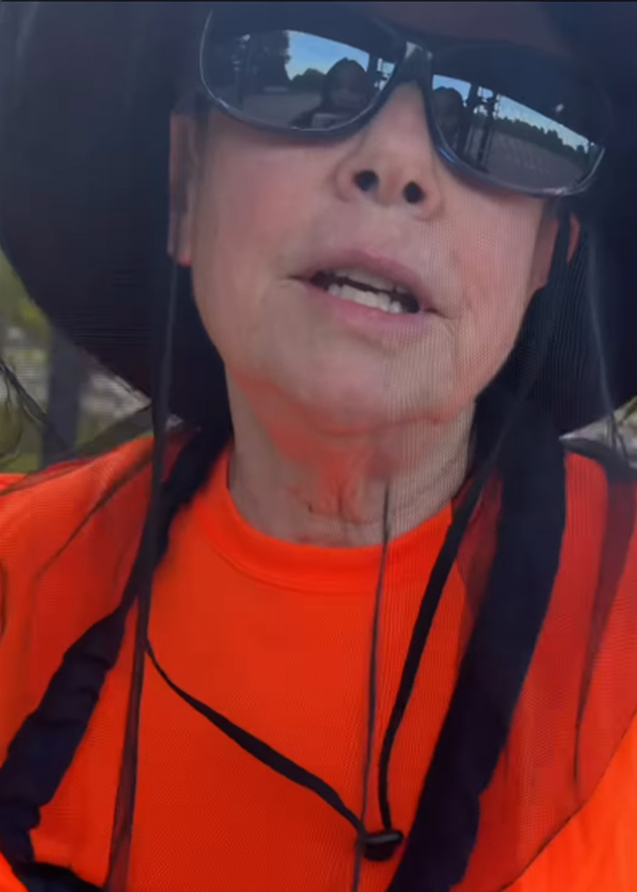 Close-up of woman in orange shirt and black hat behind mesh at field gate Close-up of woman in orange shirt and black hat behind mesh at field gate