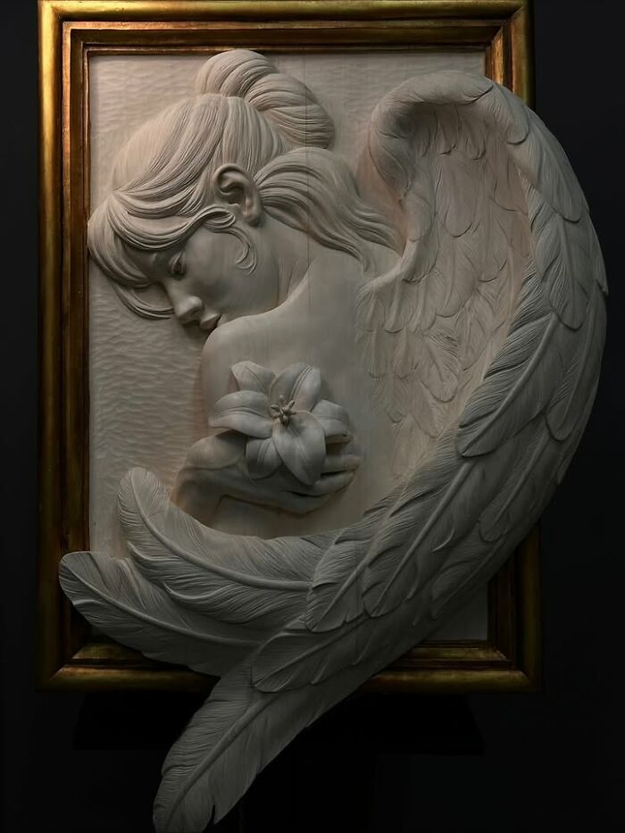 A lifelike wood sculpture of a winged woman holding a lily flower, carved into a framed panel by a Polish artist