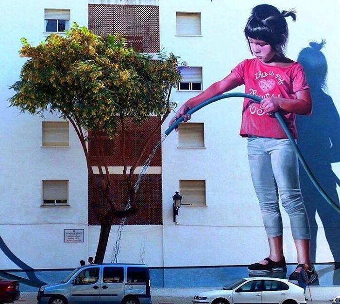 Giant girl watering a tree, an example of stunning street art on a building facade.