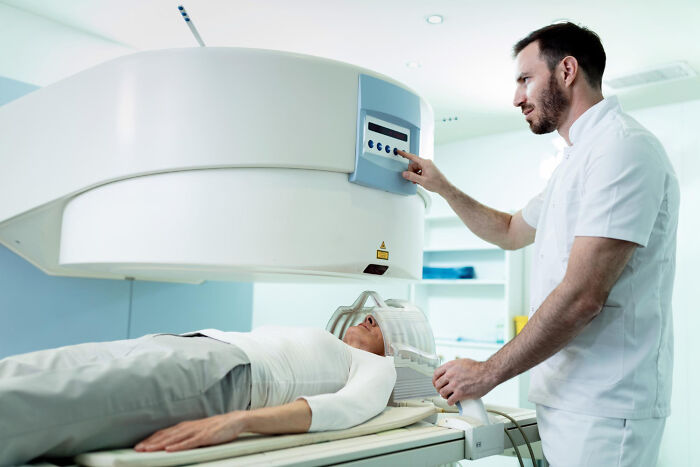A male medical professional operating a machine while a patient lies on a bed, addressing problems society faces.