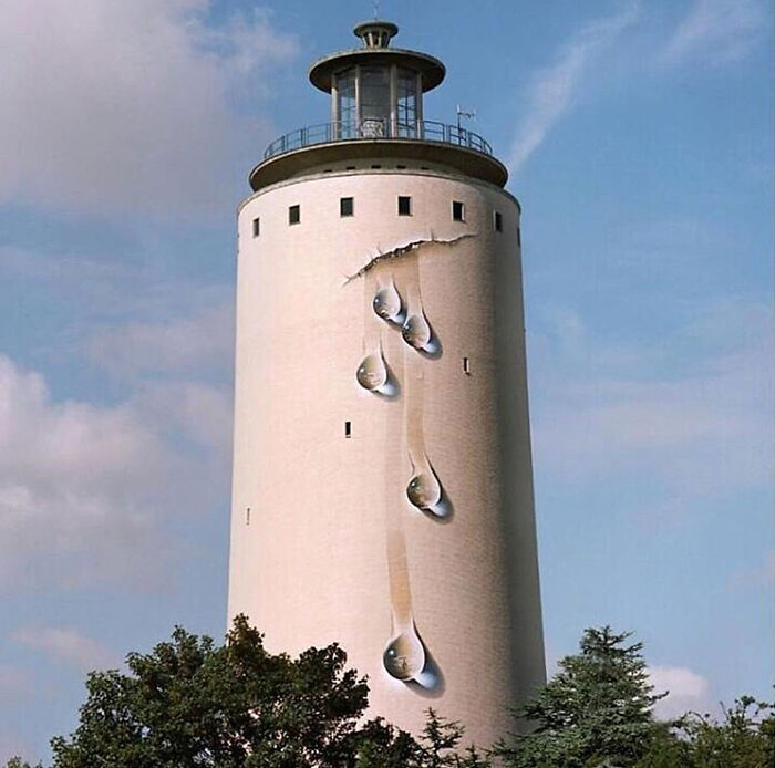 A tall white lighthouse with 3D street art of large water drops seemingly dripping down its side, stunning examples of street art.