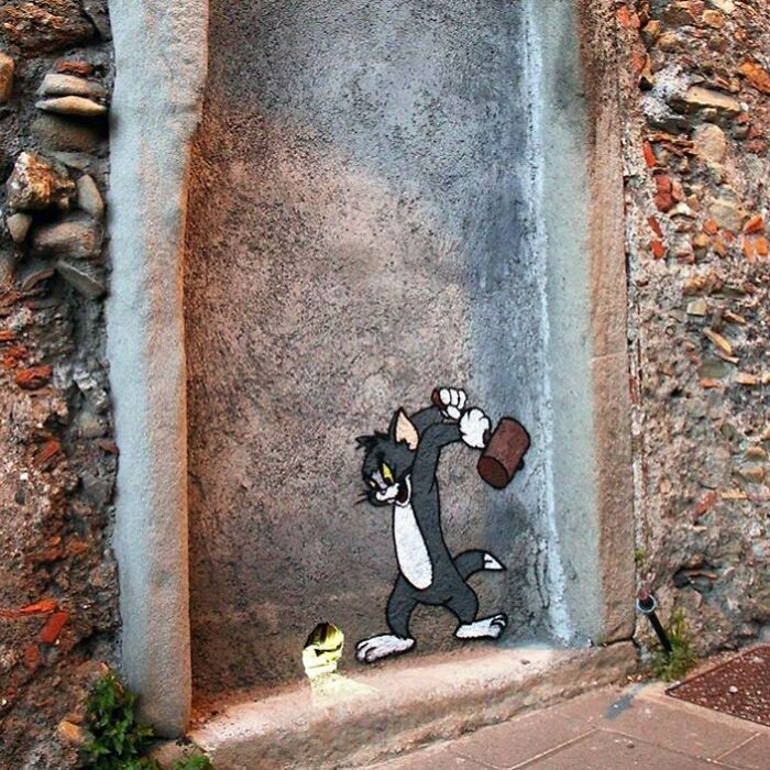 Tom from Tom and Jerry cartoon street art, holding a hammer, on a textured stone wall, showcasing stunning street art.