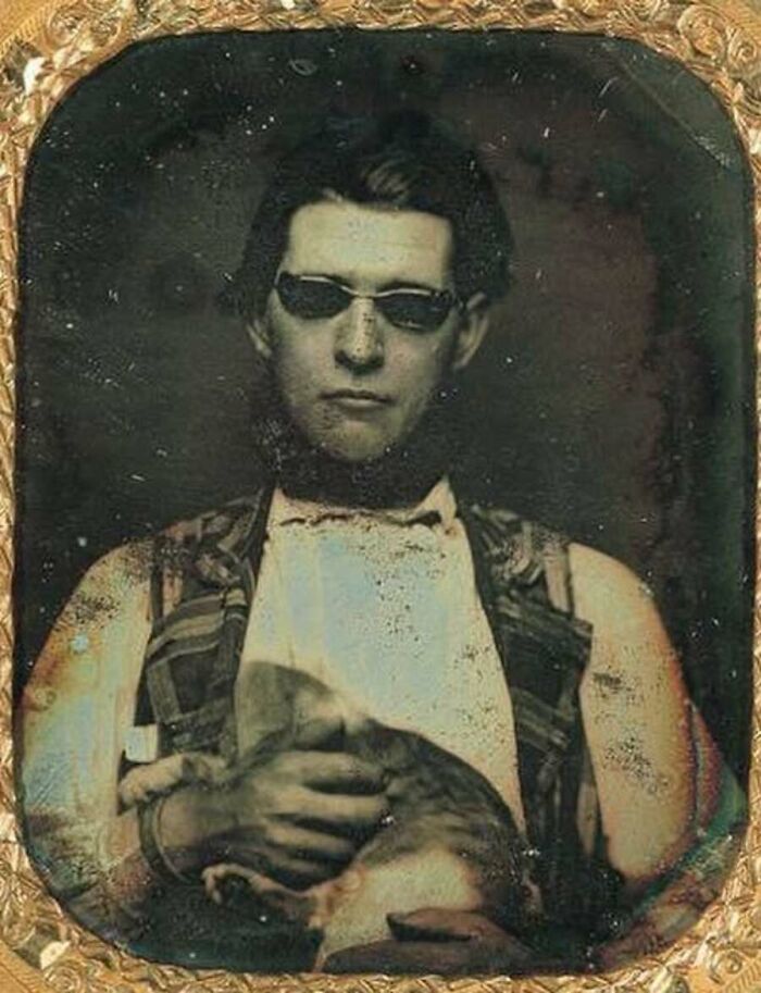 An antique daguerreotype portrait of a man in sunglasses holding a cat, representing old photos of animals