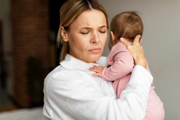A stressed woman holding a baby, feeling like a bad aunt for not putting her life on hold.