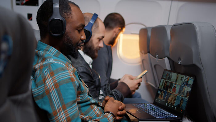 Passengers on an airplane, one watching a laptop. Highlights the experience of airline seating lottery and different seatmate stories.