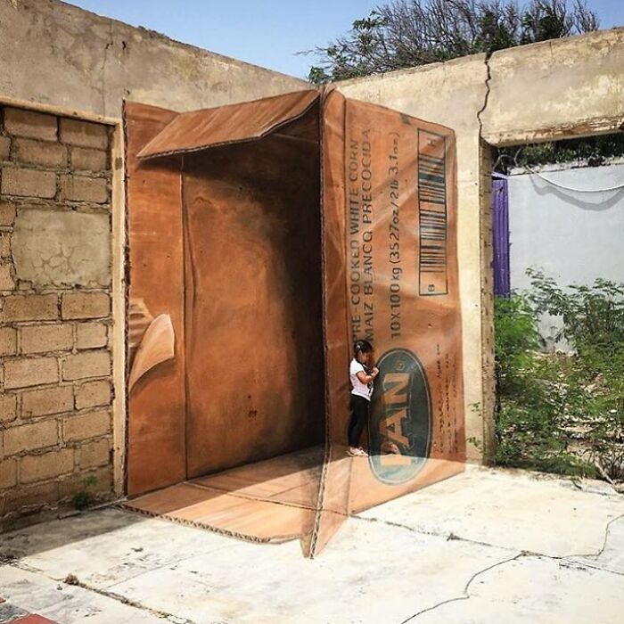 A little girl standing inside a large 3D street art mural of an open cardboard box, displaying stunning examples of street art.