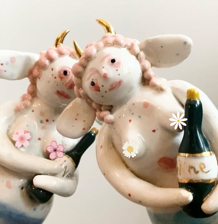 Two horned ceramic sculptures representing whimsical figures holding small wine bottles.