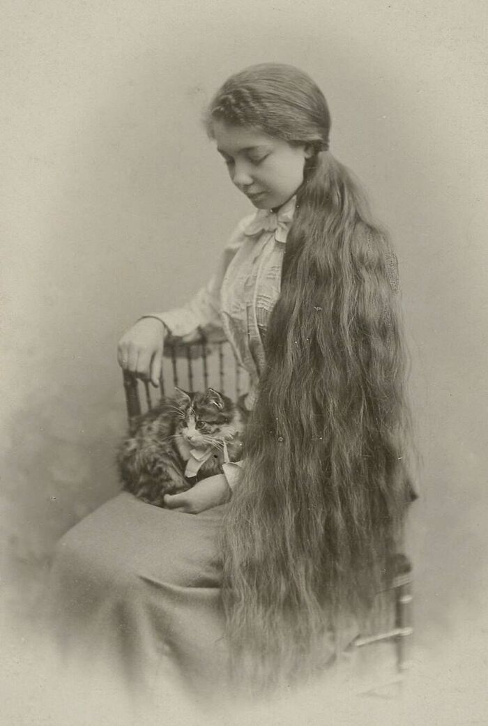 A young woman with very long hair holding her pet cat, from old photos of animals