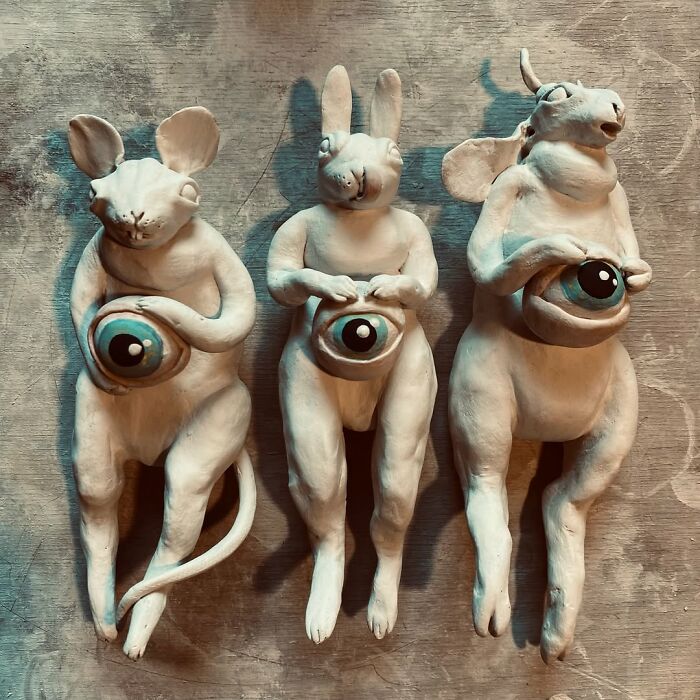 Three white ceramic sculptures representing hybrid animal figures holding large blue eyeballs.