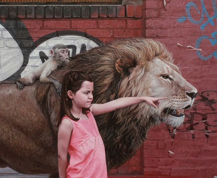 Dystopian painting by Kevin Peterson showing a young girl, a monkey, and a lion by a brick wall with graffiti