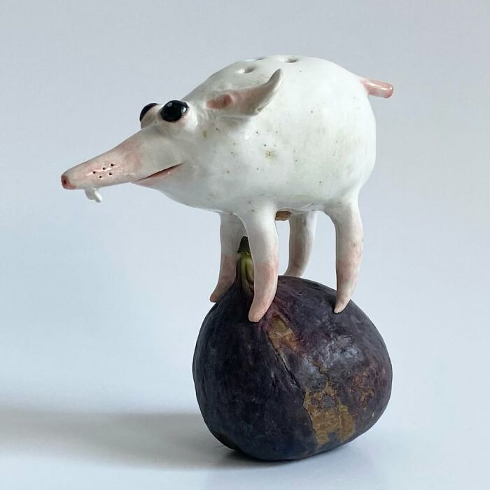 Weird ceramic sculptures creature standing on top of a dark fig as home decor