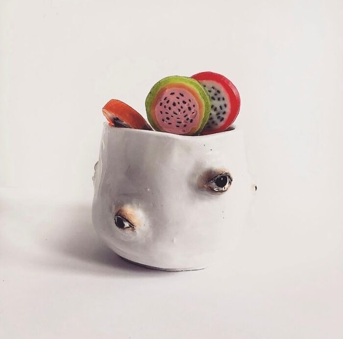 Weird ceramic sculpture holder with tiny eyes, filled with colorful clay fruit slices.