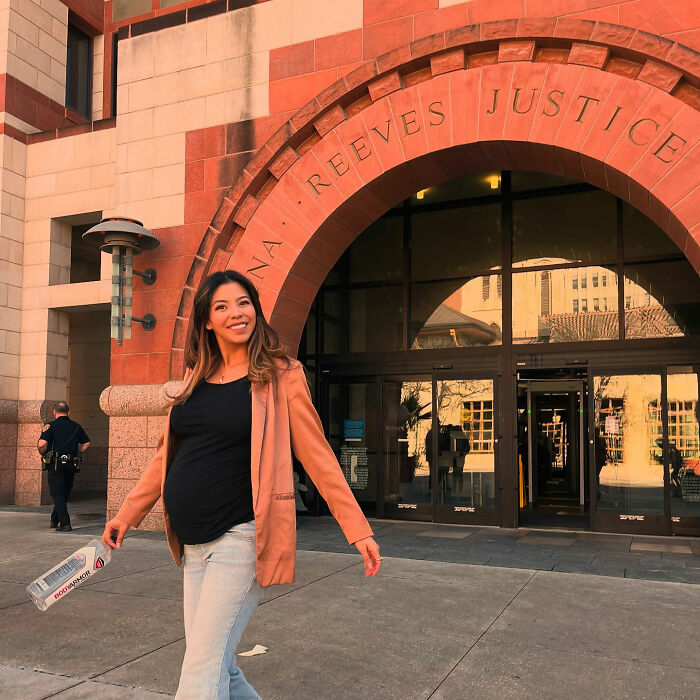 A pregnant lawyer in a stylish blazer smiling outside a courthouse, addressing the inappropriate dress issue