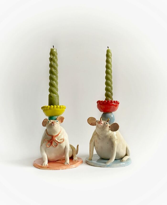 Two weird ceramic sculptures of chubby pig-like creatures holding candles on their heads.