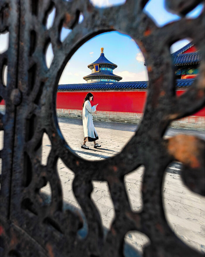A photographer frames minimalist architecture, showing a person walking past a traditional building through an ornate gate.