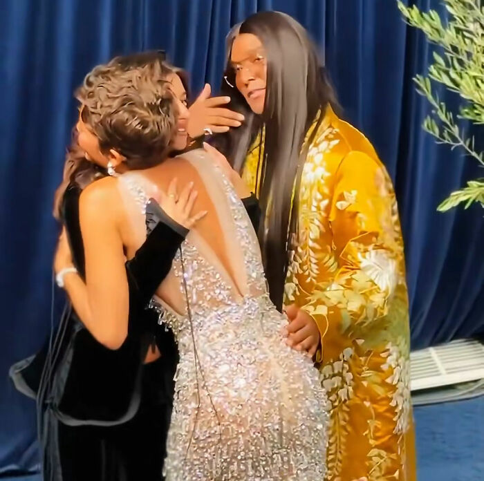 Hollywood Star in a black dress hugging Zendaya while her stylist gives an awkward interaction expression.