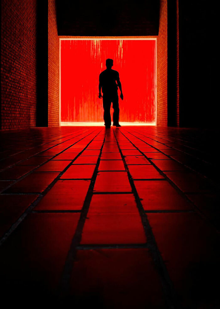 A photographer captures minimalist architecture with a silhouetted person against a striking red backdrop in an everyday scene.