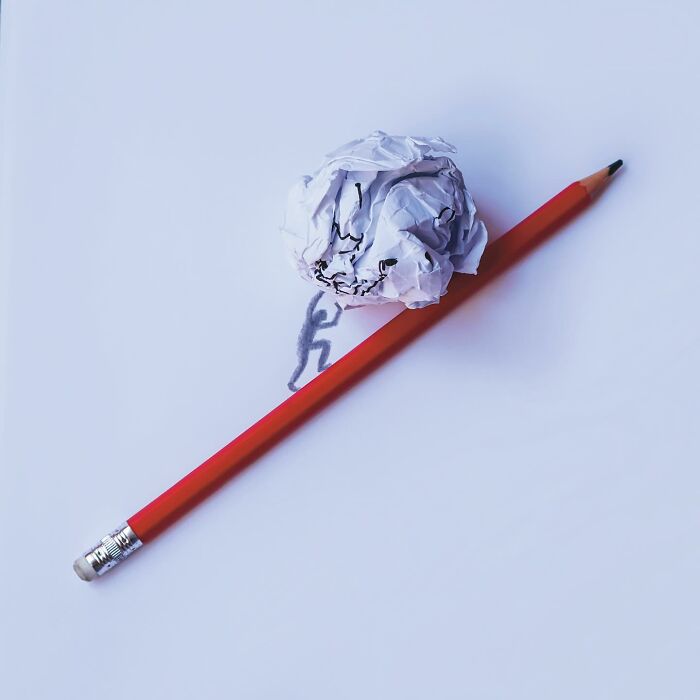 A red pencil and crumpled paper forming a playful illustration of a person carrying a heavy boulder