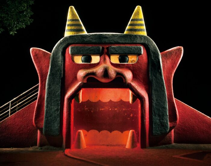 A vibrant red demon-shaped Japanese playground structure at night, captured by Fujio Kito, looking like another world scene.