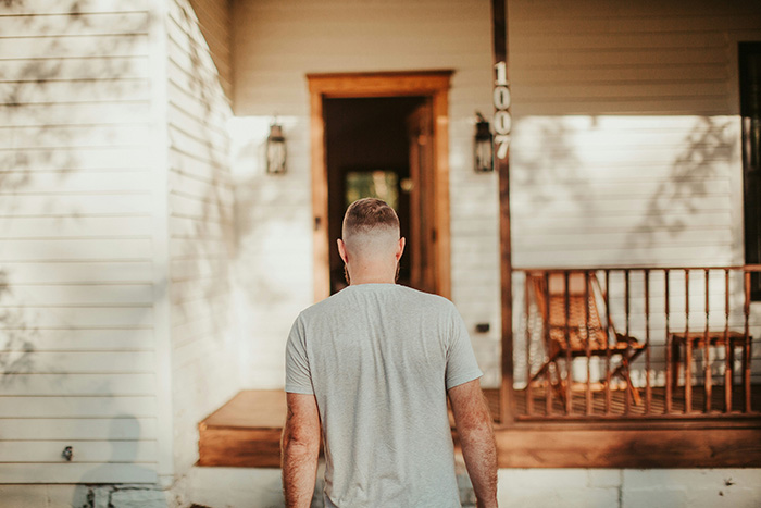 A man from behind walking towards the front door of a house representing a partner returning home A man from behind walking towards the front door of a house representing a partner returning home