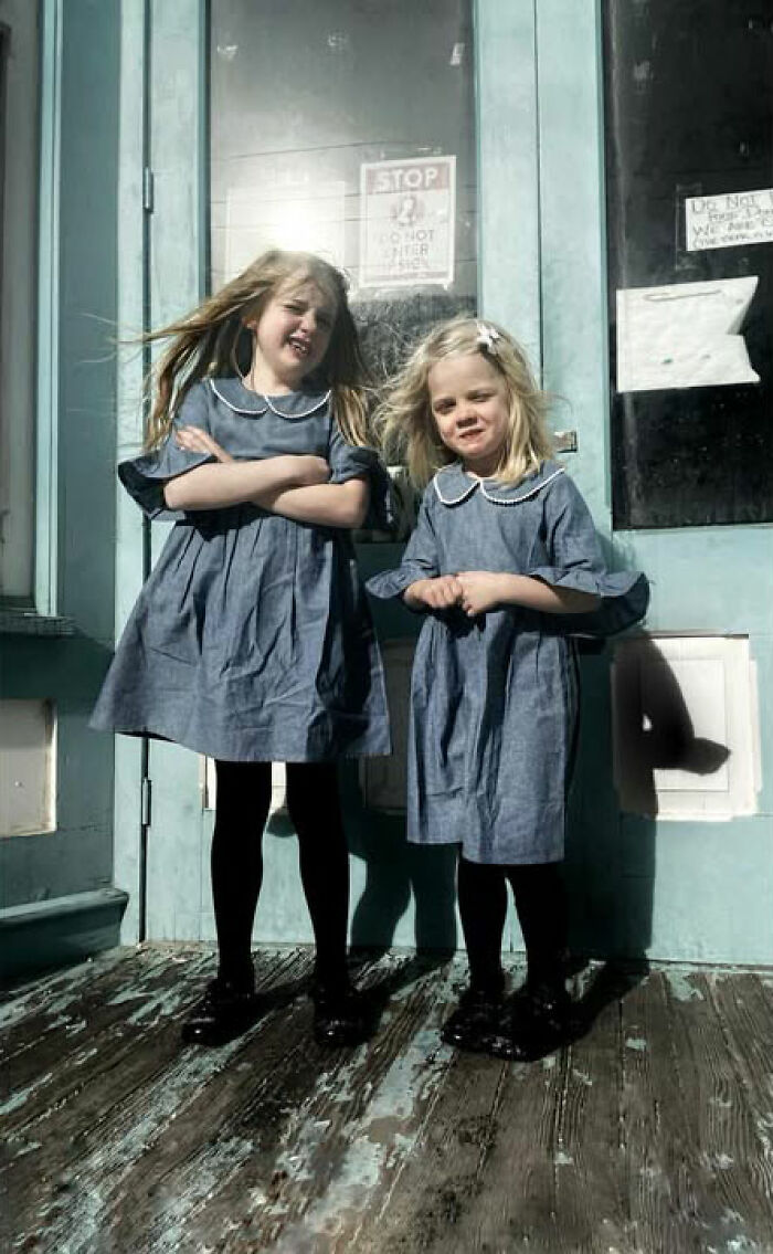 Two young girls in matching dresses stand on a weathered porch in a street photo by Taylor Coble.