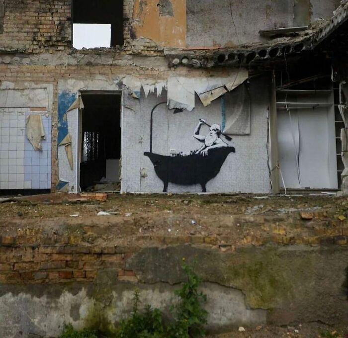 An abandoned building with powerful street art depicting a figure in a bathtub amidst the ruins.