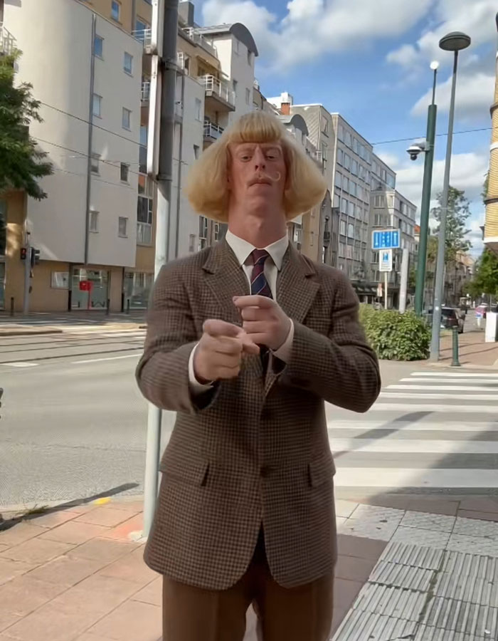 A mysterious influencer in a brown suit poses outdoors on a city sidewalk