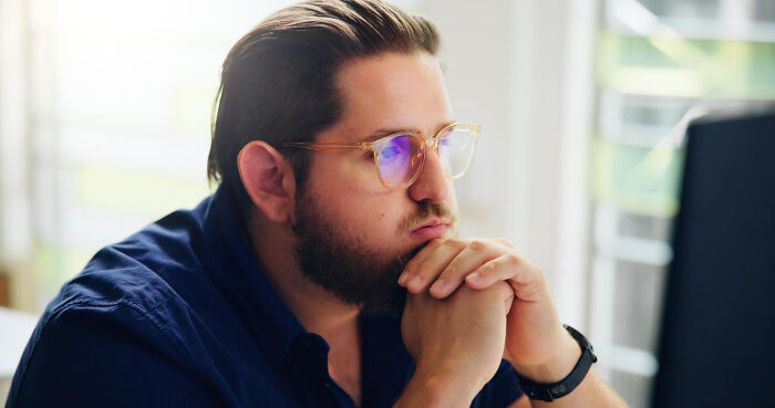 Man with a beard and glasses intently looking at a screen, considering problems society could face.