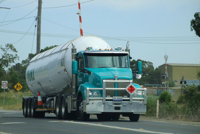 A large teal tanker truck driving on a road, a common sight that can spark weird childhood beliefs.