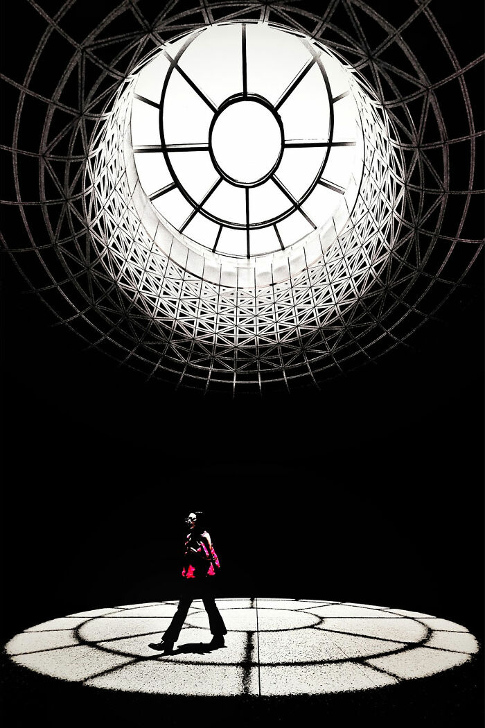 A photographer's minimalist architecture scene features a person silhouetted beneath a large, intricate circular skylight.