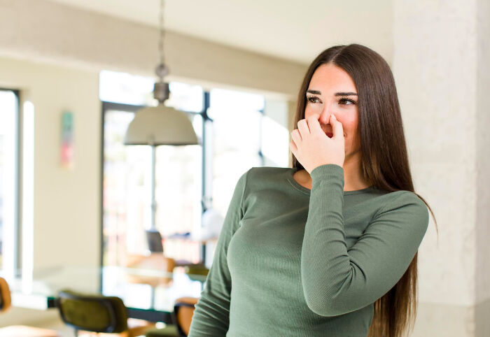 A woman pinching her nose, reacting to an unpleasant smell, a common scenario in pure nightmare seatmate stories from airline seating.