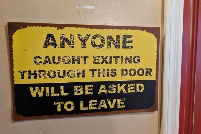 A funny sign that says Anyone caught exiting through this door will be asked to leave, a silly warning.