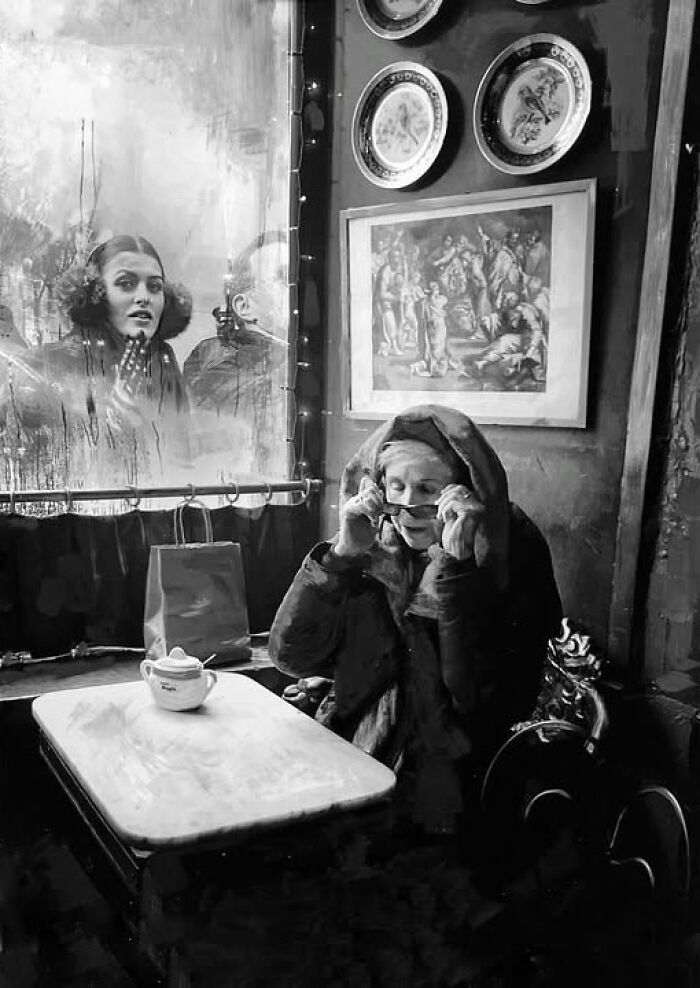 A dramatic black and white street photo by Taylor Coble of a woman in a cafe, obscuring her face, with reflections.