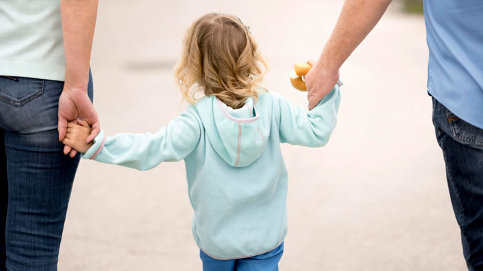 A young child holding hands with two adults, representing a mother leaving children to pursue IVF. A young child holding hands with two adults, representing a mother leaving children to pursue IVF.