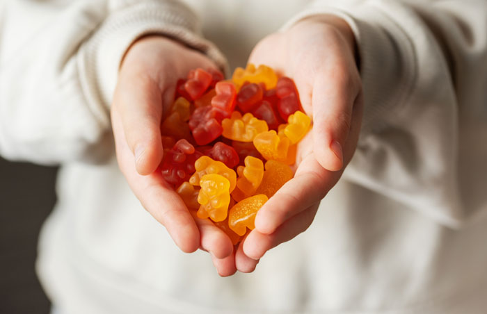 Hands holding a pile of colorful gummy bears, representing viral Ashwagandha gummies linked to liver failure.