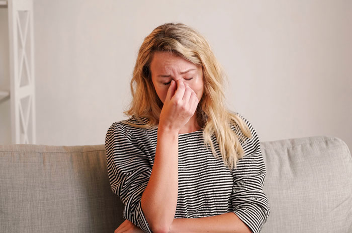 A distraught wife is crying, holding her nose and forehead, reflecting her marriage breaking point after hubby's flirting.