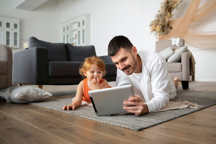 A father and young child happily watch a tablet. A mother sparks outrage for leaving children for IVF. A father and young child happily watch a tablet. A mother sparks outrage for leaving children for IVF.