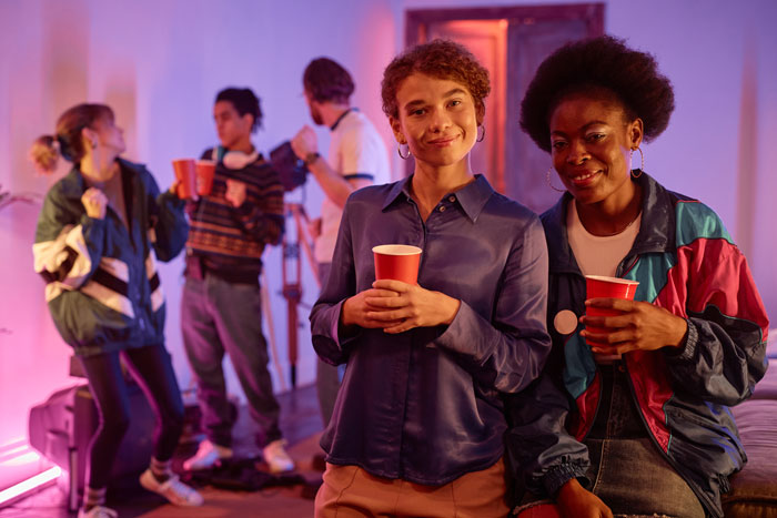 Two students holding red cups at a loud party, while other students dance in the background. Two students holding red cups at a loud party, while other students dance in the background.
