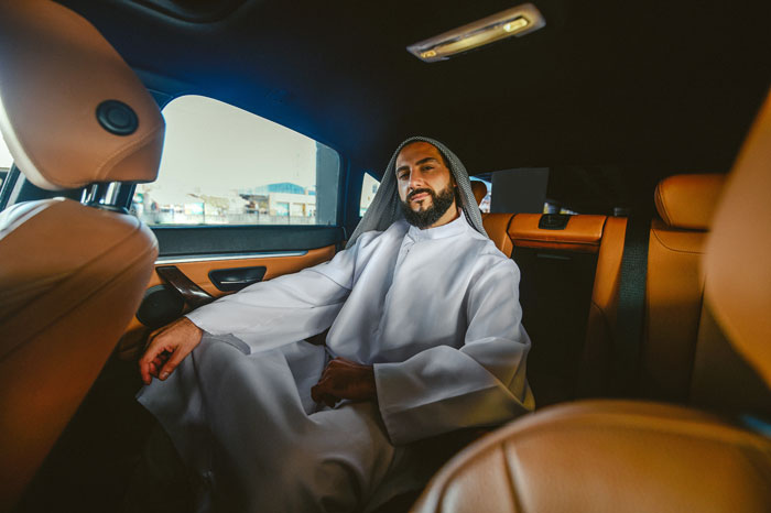 A wealthy man in traditional attire sits comfortably in the back of a luxurious car, representing things wealthy people buy.