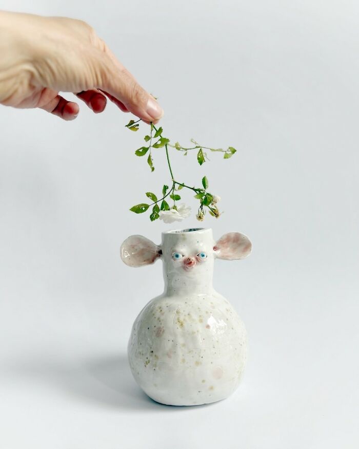 A hand putting a flower in a weird ceramic vase shaped like a pig-nosed creature