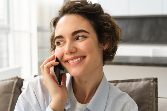 A woman smiling while talking on a cell phone, perhaps doing crazy things to get a crush to like her.