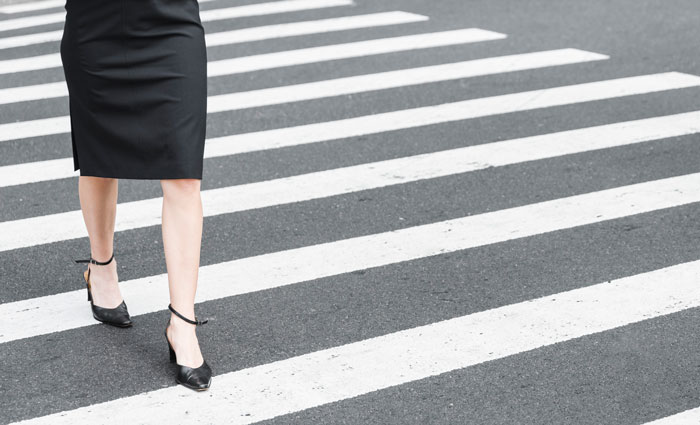 A person in a black skirt and heels walks on a zebra crossing, symbolizing karma and justice.