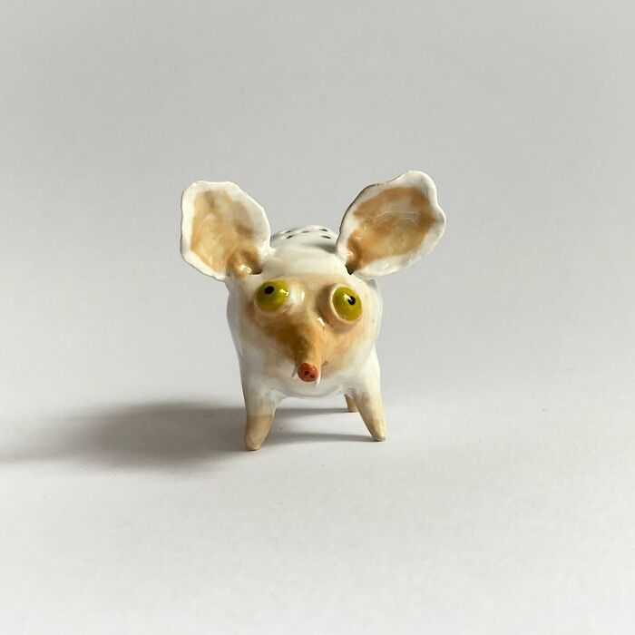 A tiny, quirky ceramic sculpture of a white and yellow creature with big round eyes and ears.