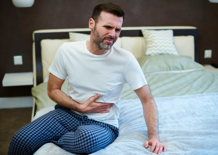 Man holding stomach in pain sitting on bed indicating internal discomfort